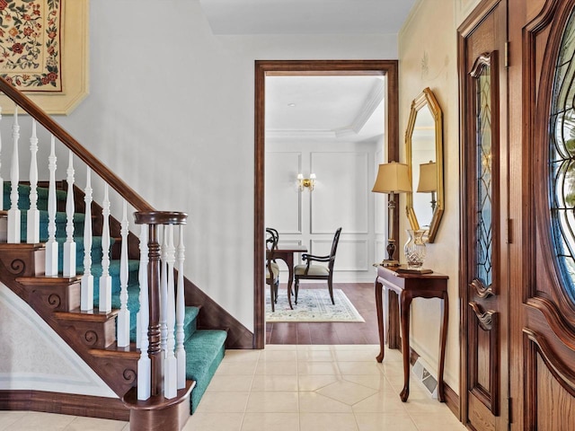 foyer entrance with light tile patterned floors, stairway, a decorative wall, and ornamental molding