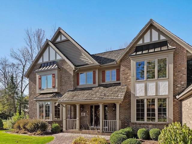 rear view of house featuring metal roof, brick siding, a standing seam roof, and a porch