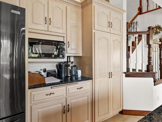 kitchen with black microwave, baseboards, cream cabinetry, fridge, and dark stone countertops