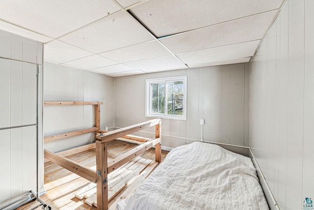 bedroom with a drop ceiling, wood walls, and wood-type flooring