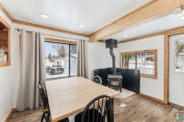 dining space featuring a wood stove, baseboards, beamed ceiling, and hardwood / wood-style floors