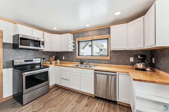 kitchen featuring a sink, wooden counters, appliances with stainless steel finishes, light wood-type flooring, and decorative backsplash