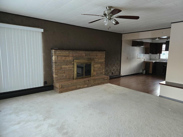 unfurnished living room with ceiling fan, carpet floors, a stone fireplace, and wood finished floors