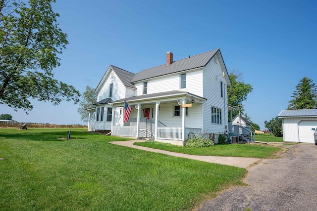 view of front of house featuring a chimney, a porch, a front yard, metal roof, and an outdoor structure