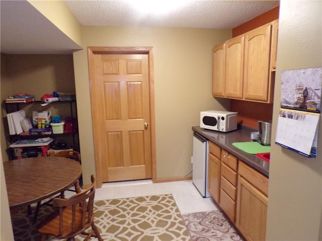 kitchen with white microwave, dark countertops, light brown cabinets, light tile patterned floors, and a textured ceiling