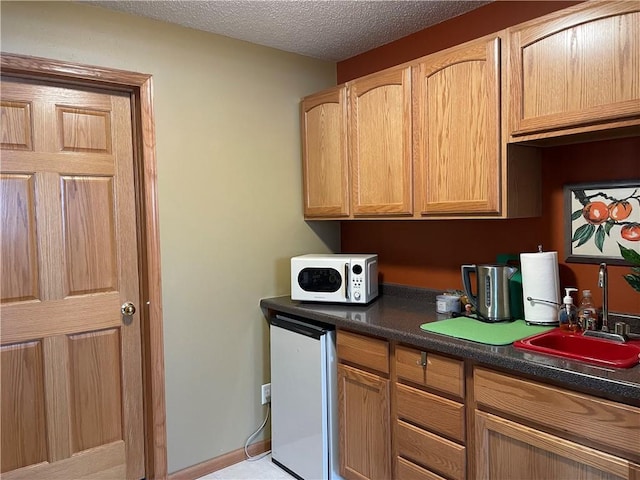 kitchen with white microwave, dark countertops, refrigerator, a textured ceiling, and a sink