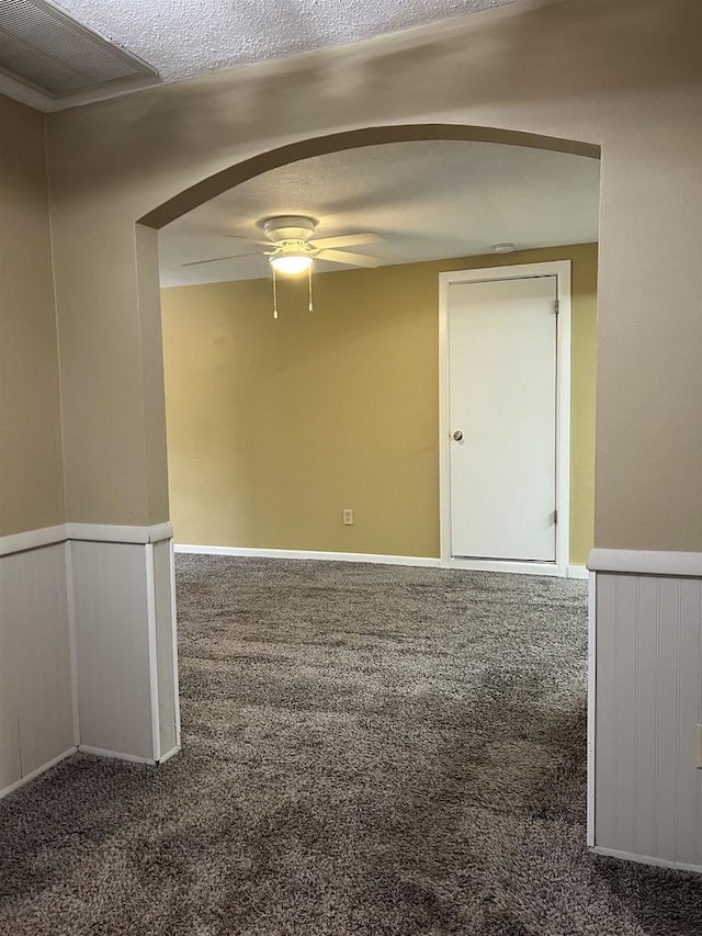 unfurnished room with a wainscoted wall, a ceiling fan, a textured ceiling, arched walkways, and carpet