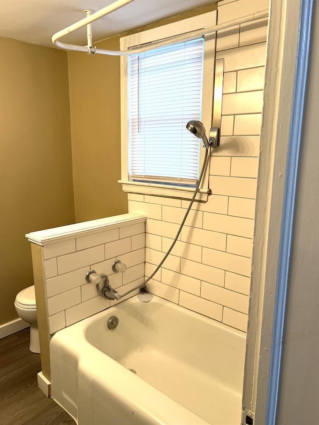 bathroom featuring toilet, a bath, wood finished floors, and baseboards