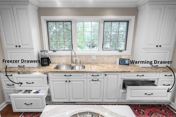 kitchen featuring white cabinetry, crown molding, and a sink