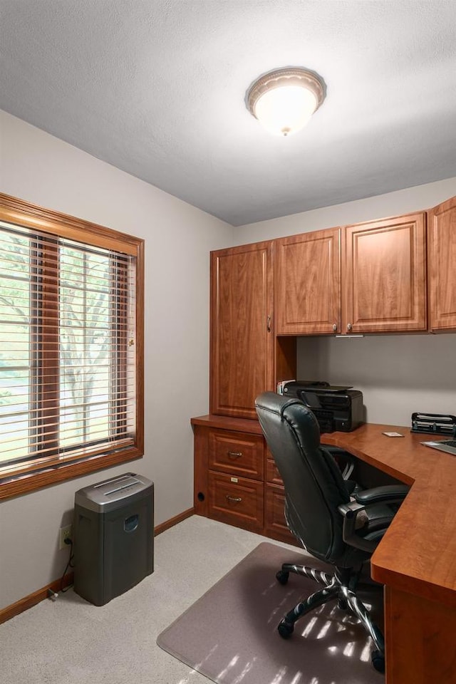 office featuring light carpet, built in desk, a textured ceiling, and baseboards