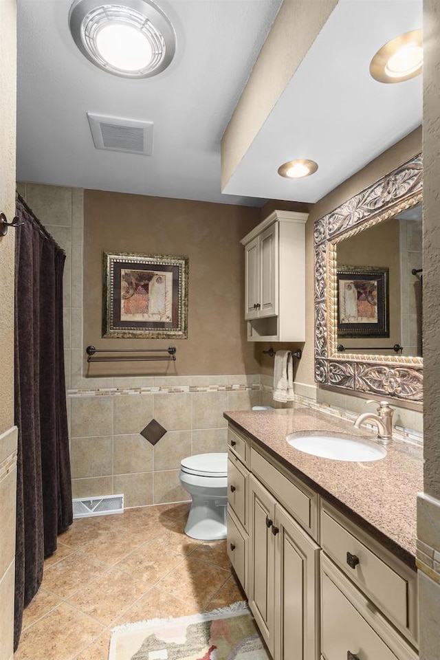 bathroom with tile patterned flooring, visible vents, toilet, vanity, and tile walls