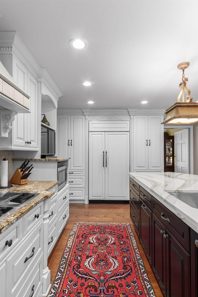 kitchen with dark brown cabinetry, built in appliances, recessed lighting, light wood-style floors, and white cabinetry