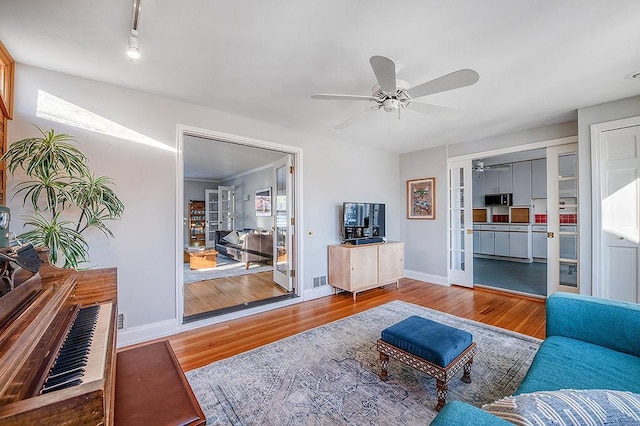 living room featuring ceiling fan, french doors, baseboards, and wood finished floors