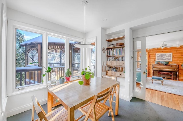 dining area with baseboards, finished concrete floors, wood walls, and a ceiling fan