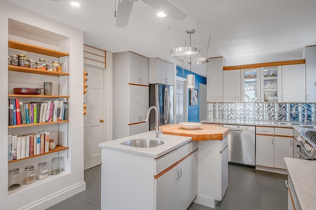 kitchen with a center island with sink, a sink, decorative light fixtures, white cabinetry, and appliances with stainless steel finishes