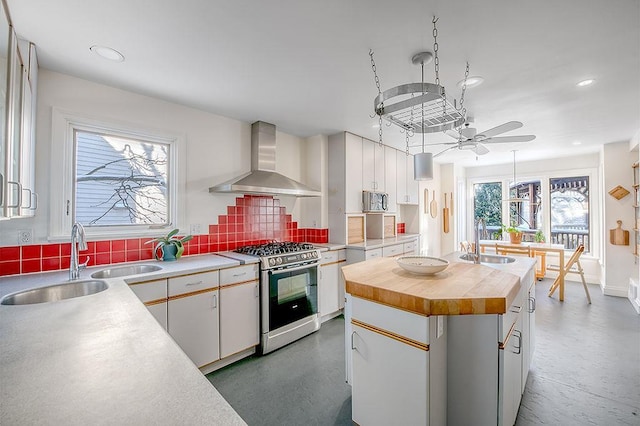 kitchen with stainless steel gas stove, butcher block countertops, a sink, backsplash, and wall chimney range hood