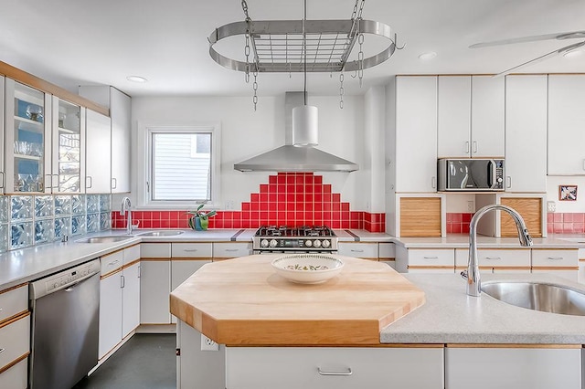 kitchen with backsplash, appliances with stainless steel finishes, wall chimney range hood, and a sink