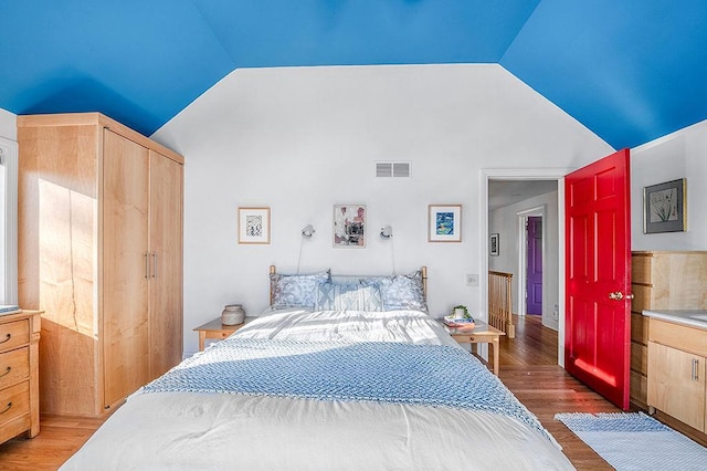 bedroom featuring vaulted ceiling, wood finished floors, visible vents, and a closet