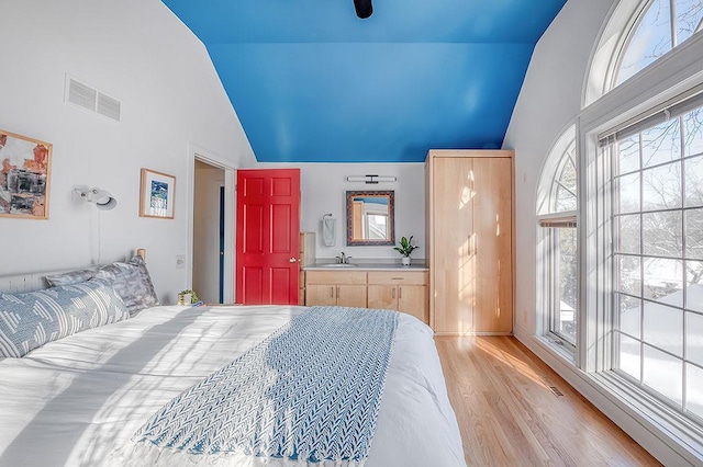 bedroom featuring high vaulted ceiling, light wood-style floors, visible vents, and a sink