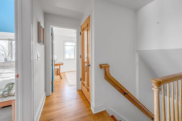 hallway with baseboards, an upstairs landing, and light wood finished floors