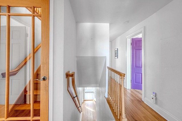 hall featuring wood finished floors, an upstairs landing, and baseboards