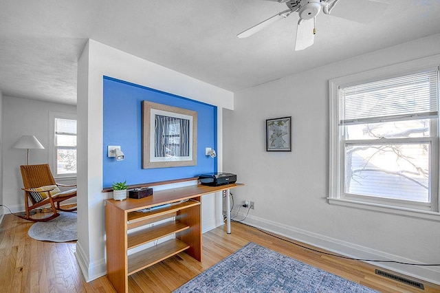 office area with visible vents, a ceiling fan, light wood-type flooring, and baseboards