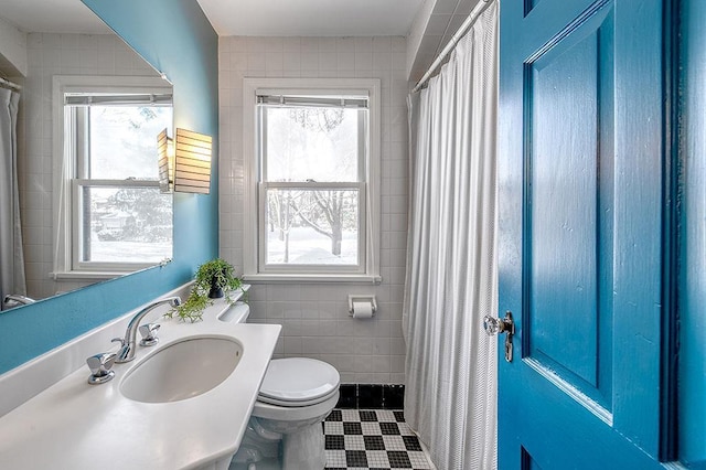 full bath with tile walls, toilet, a healthy amount of sunlight, and a sink