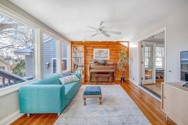 living area with wooden walls, a ceiling fan, wood finished floors, baseboards, and track lighting