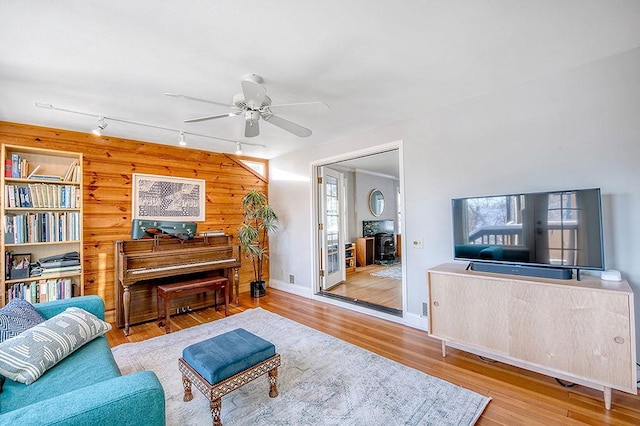 living room featuring baseboards, ceiling fan, wood walls, rail lighting, and wood finished floors