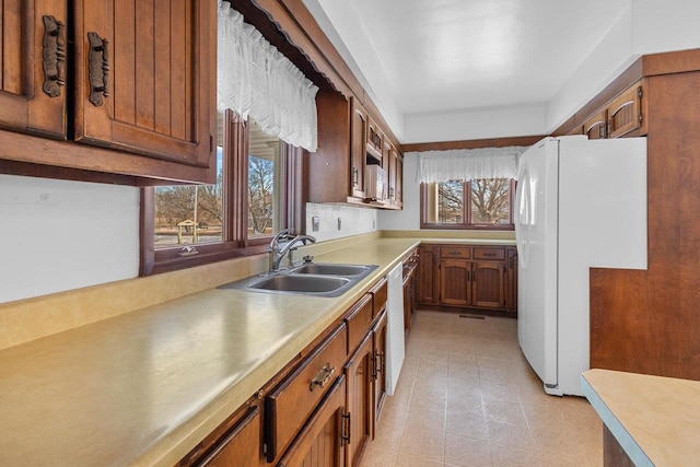kitchen featuring brown cabinets, white appliances, light countertops, and a sink