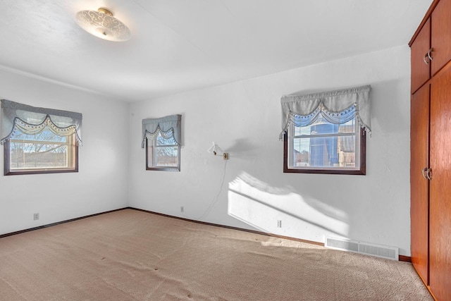 unfurnished room with a wealth of natural light, visible vents, baseboards, and carpet floors