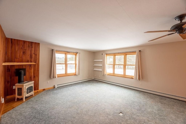 unfurnished living room with carpet flooring, wood walls, a wood stove, and ceiling fan