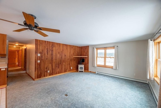 unfurnished living room featuring wooden walls, a baseboard heating unit, a wood stove, and carpet floors