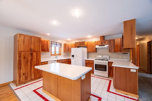 kitchen with white appliances, brown cabinetry, a sink, light countertops, and under cabinet range hood