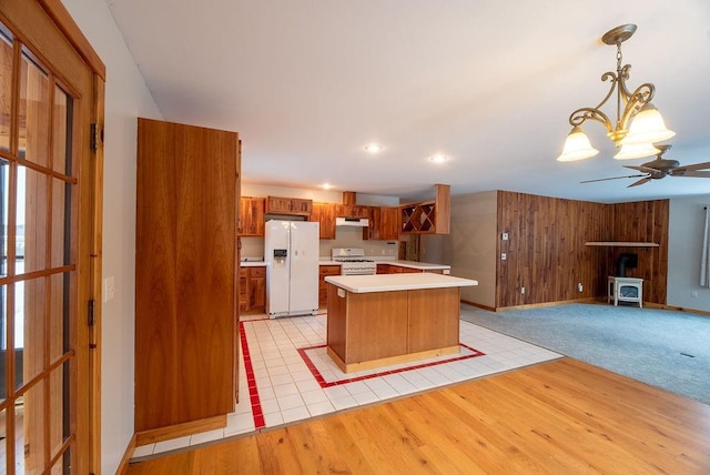 kitchen featuring white appliances, light wood finished floors, a wood stove, light countertops, and under cabinet range hood