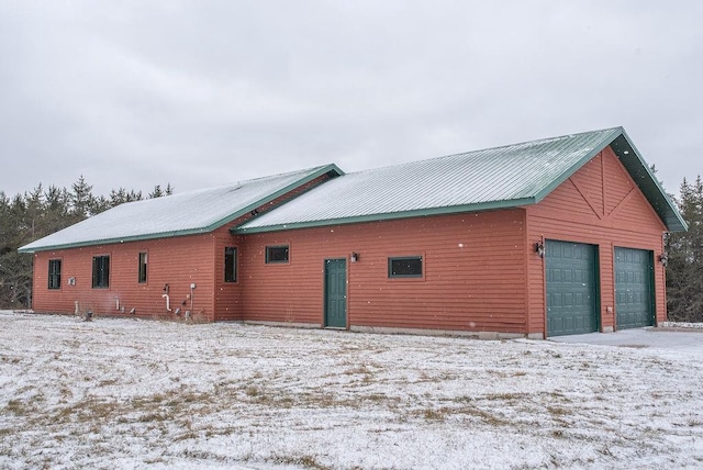 view of snowy exterior with a garage and metal roof