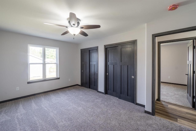 unfurnished bedroom featuring carpet, baseboards, two closets, and ceiling fan