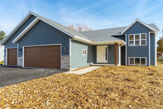 split level home featuring stone siding, an attached garage, roof with shingles, and driveway