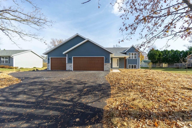 single story home featuring aphalt driveway, stone siding, and an attached garage