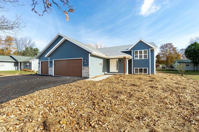 tri-level home featuring aphalt driveway, stone siding, and an attached garage