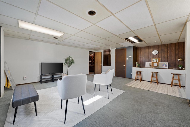 living area with a paneled ceiling, light carpet, and wood walls