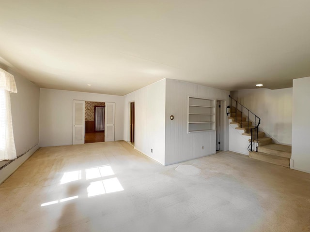 unfurnished room featuring light colored carpet and stairs