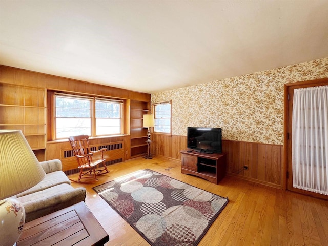 unfurnished living room featuring radiator, built in features, a wainscoted wall, wallpapered walls, and light wood-style floors