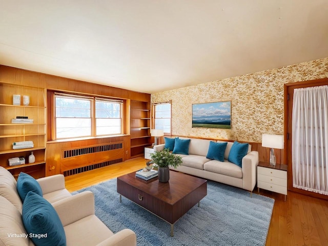 living room featuring built in shelves, wallpapered walls, radiator heating unit, and wood-type flooring