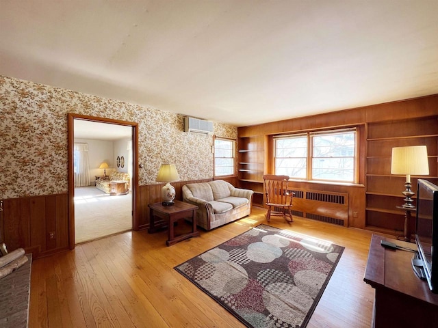 living room featuring a wall mounted AC, wallpapered walls, light wood-style flooring, radiator heating unit, and wainscoting