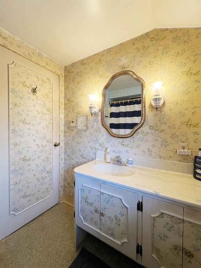 full bathroom featuring wallpapered walls, vanity, and vaulted ceiling