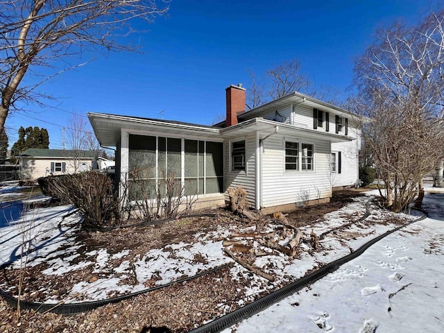 snow covered property with a sunroom and a chimney