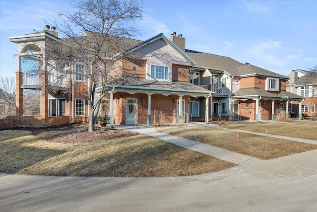 view of front of property featuring a front yard, a porch, brick siding, and a chimney