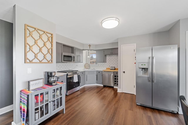 kitchen featuring dark wood-type flooring, light countertops, decorative backsplash, gray cabinets, and appliances with stainless steel finishes