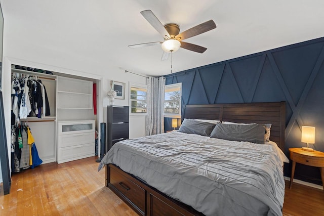 bedroom with a decorative wall, light wood-type flooring, and ceiling fan